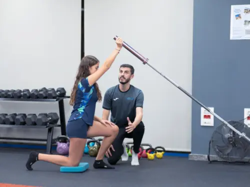 mujer con entrenador levantando barra